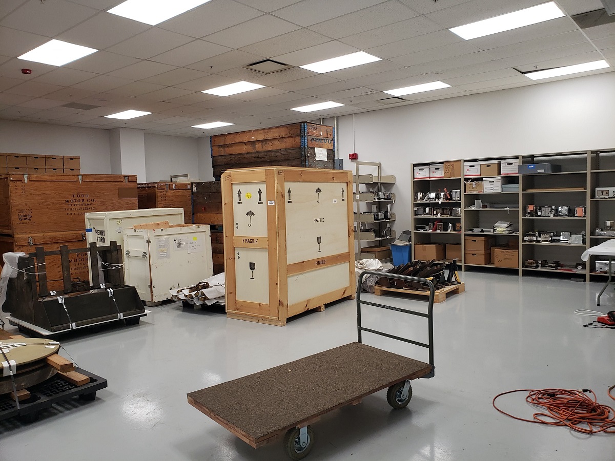 Collections in our new Photo Studio space before it was cleared and built out Room containing crates, shelving full of items, and large items on pallets