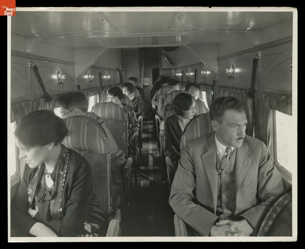 Passengers sit, one on either side of the aisle, looking out the windows of an airplane