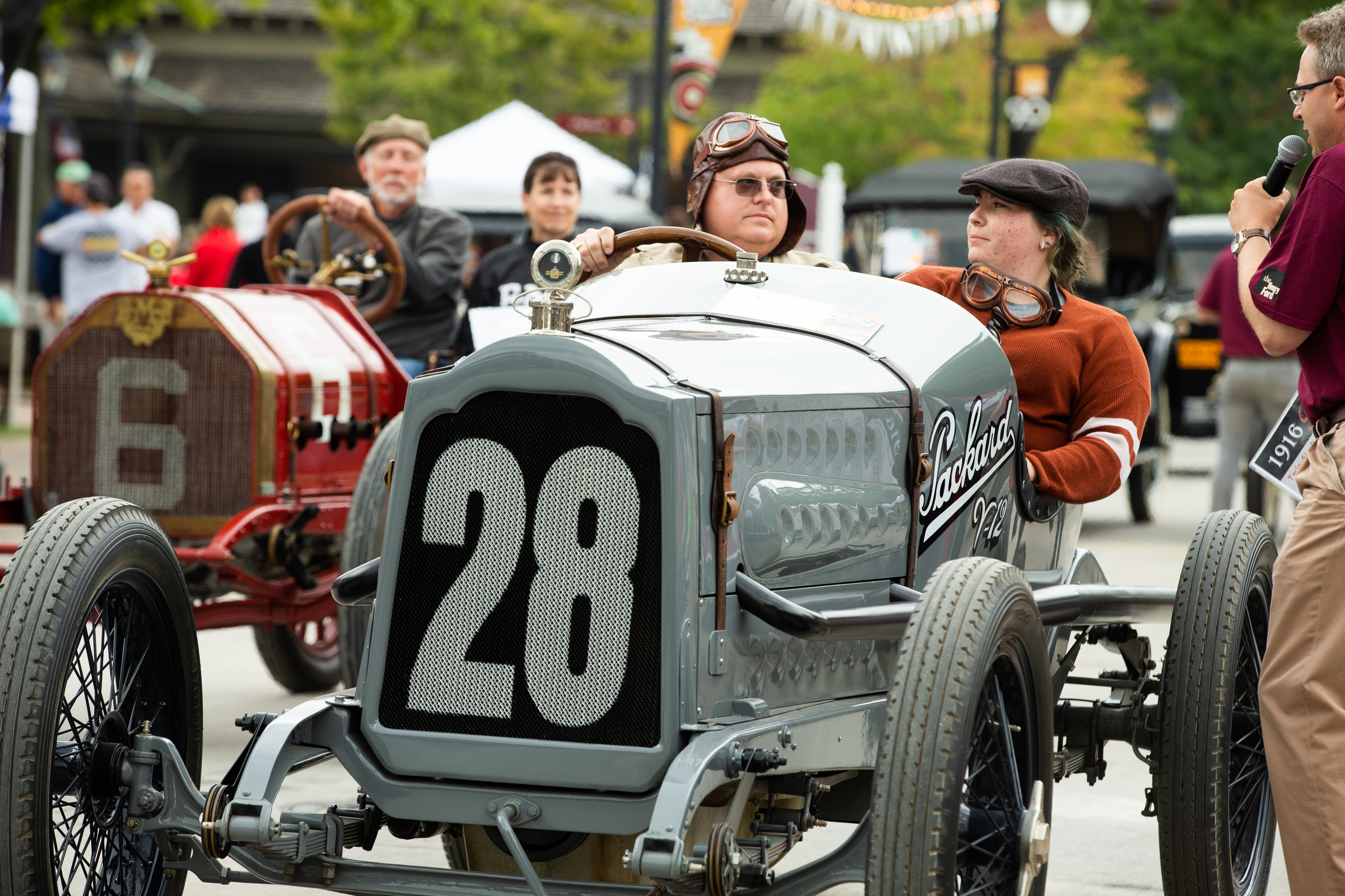 Participants and their cars at Old Car Festival Two people in vintage car in foreground and another two in another car in background; additional cars in the distance