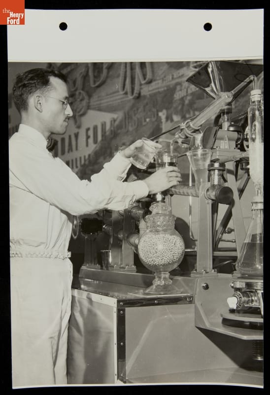 A man holds beakers of liquid up to an apparatus