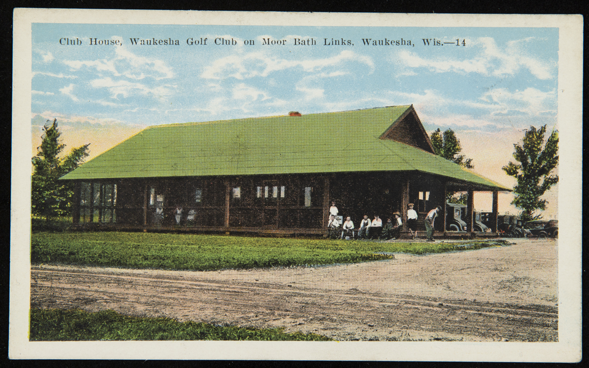Postcard of open wooden building with green roof, with people sitting and standing on porch; also contains text 