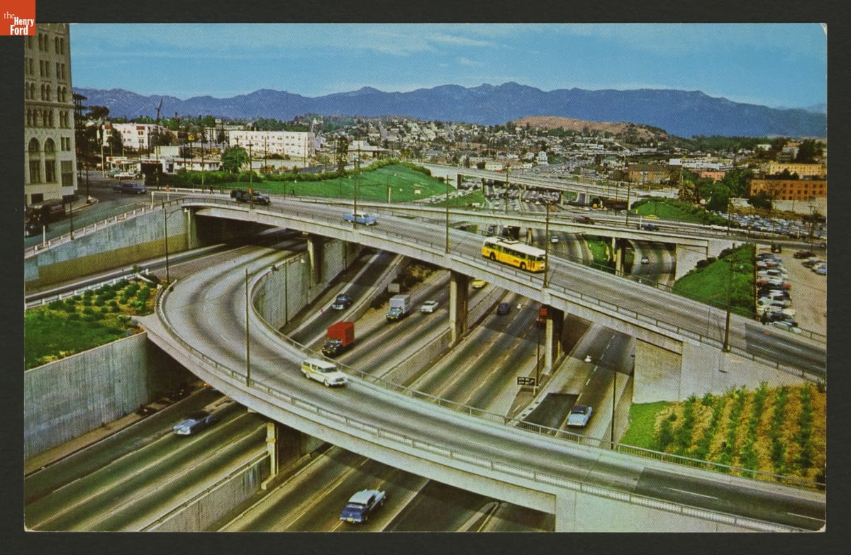 Color postcard showing a complicated curving multilevel freeway interchange with a city behind it