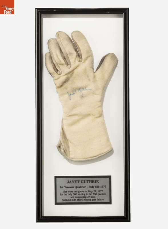 Racing Glove Worn by Janet Guthrie during the 1977 Indy 500 White or cream-colored glove with signature in blue ink in center of palm, mounted under glass in a black frame with a plaque containing text underneath