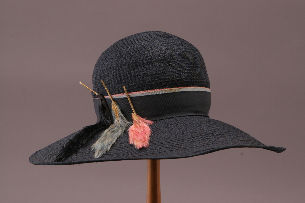 Black straw hat with black ribbon and feather detailing in black, pale blue, and pink 
