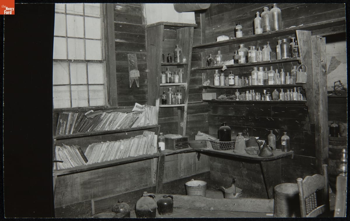 Dr. Howard's Office at Its Original Site, Tekonsha, Michigan, March 1956 Black-and-white photo of room interior with wooden walls lined with wooden shelves containing books, bottles, and jars
