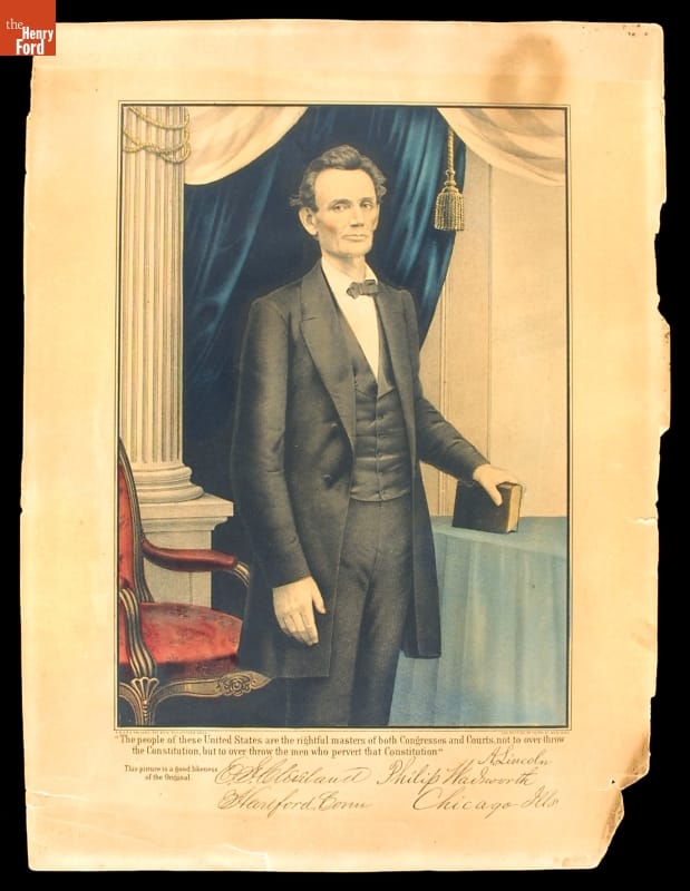 Color portrait of tall, thin man in black suit, standing before a blue curtain and holding a book
