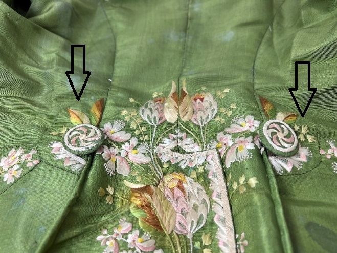 Moss-green fabric with elaborate embroidery; arrows point to two buttons covered in embroidered fabric and embroidered semicircles surrounding each