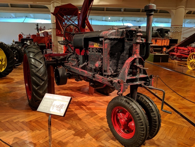 Farmall tractor before 2019 conservation project Tractor on wood floor in exhibit, surrounded by other equipment