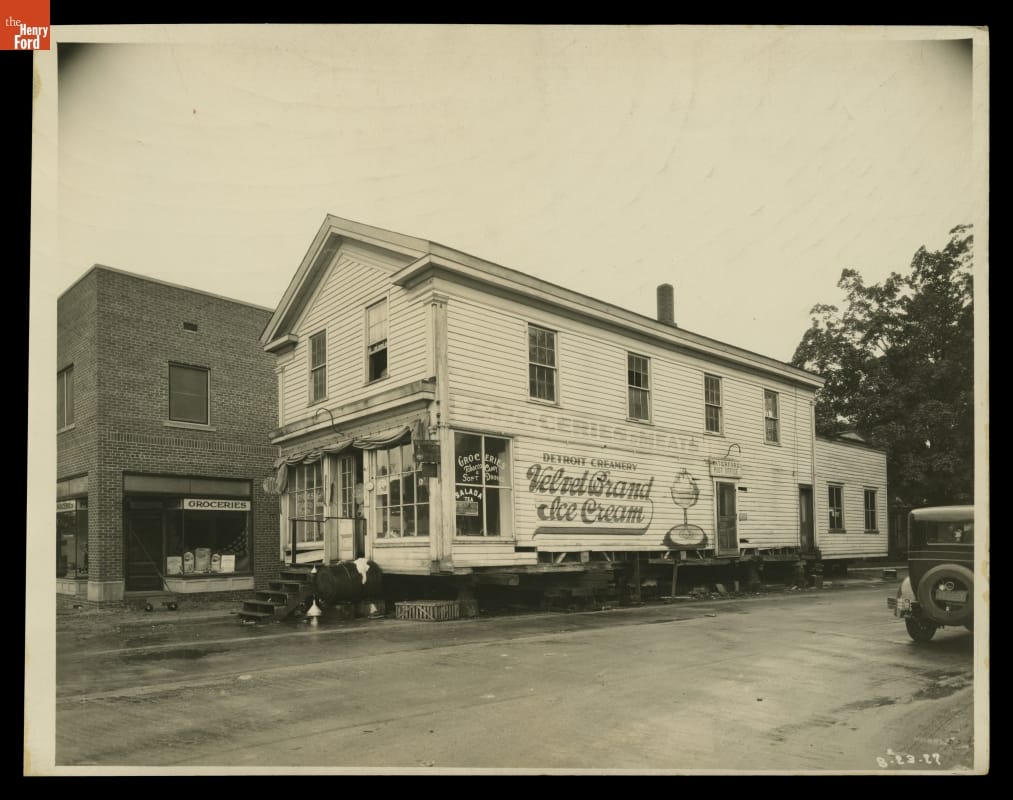 Two story wooden building with mural on side, elevated slightly on jacks