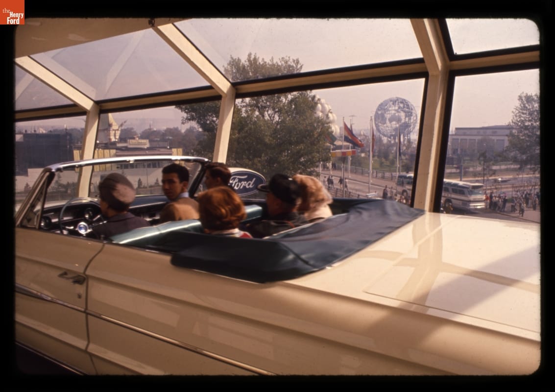 Car in Transparent Tunnel of the Magic Skyway Ride, Ford Pavilion, New York World's Fair, 1964-1965 Six people sit in white convertible in a glass tunnel with a fairground visible through the windows