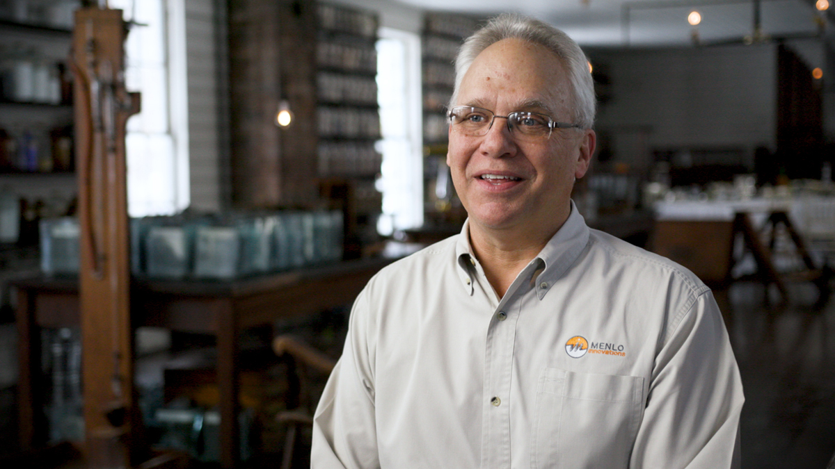 Man with white hair, white shirt, and glasses sitting in 19th century laboratory