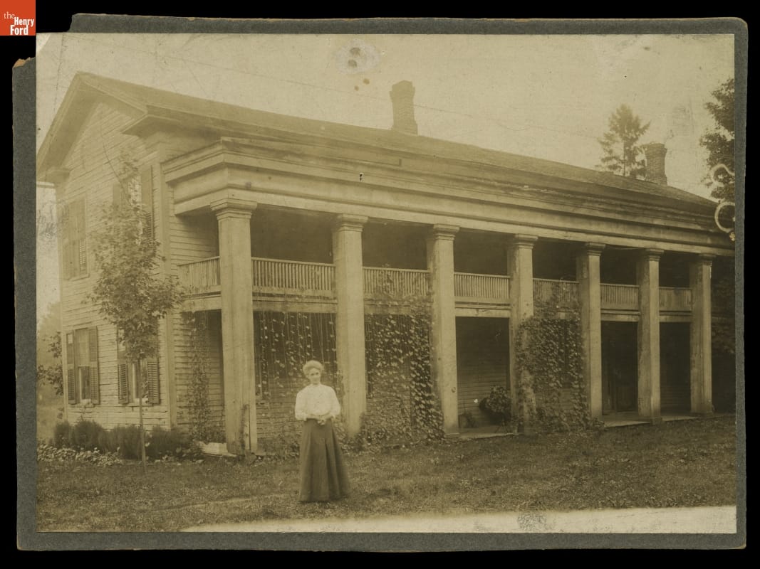 Woman stands in front of long, two-story building with columns