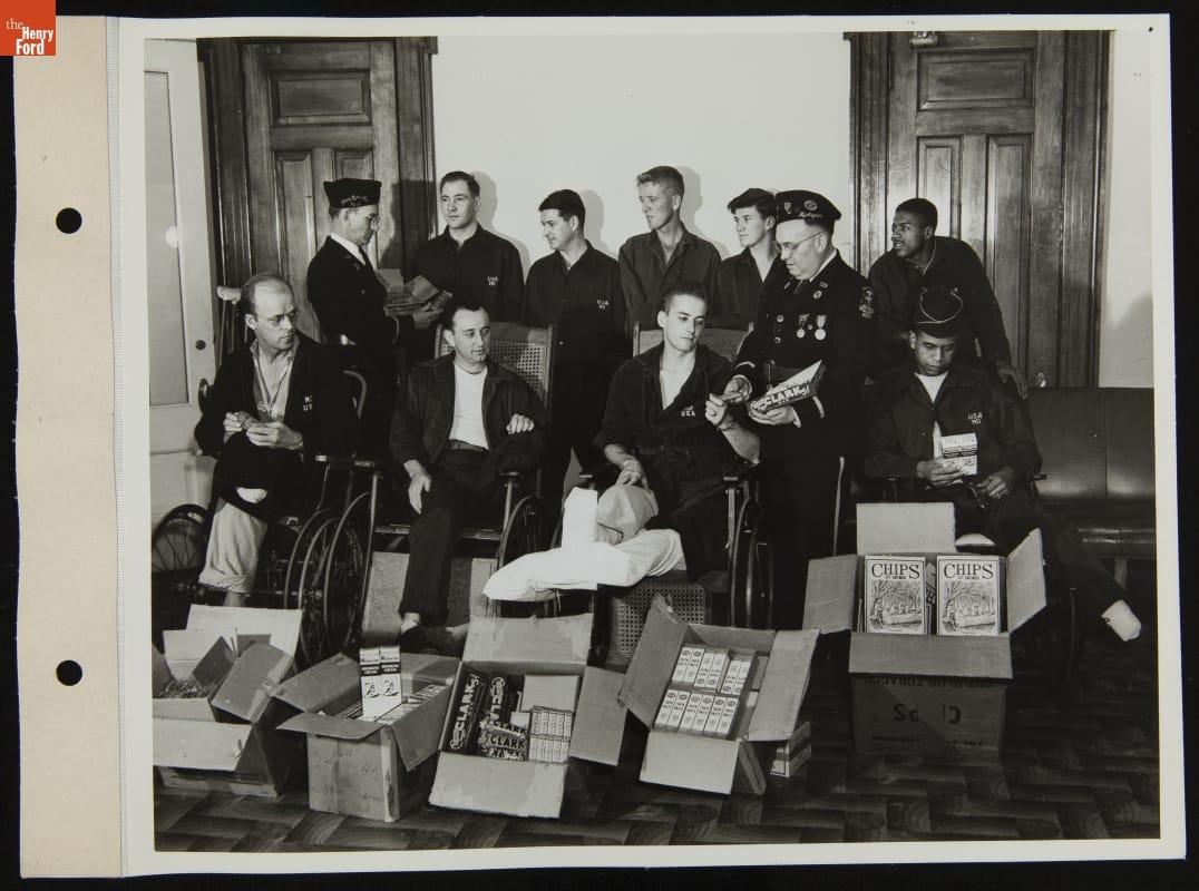 Patients at Percy Jones Hospital Receive Gifts Collected at Ford Rotunda, April 1945 Group of men in robes and pajamas, some in wheelchairs, are handed items by two soldiers; additional items in boxes in front of the group