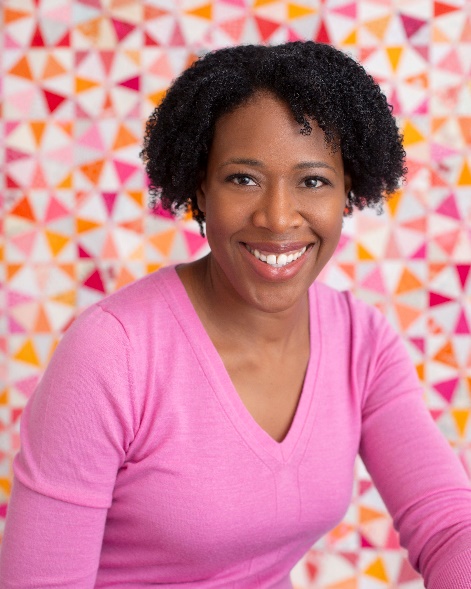 Medium-dark-skinned woman wearing pink top with bobbed curly black hair in front of a colorful backdrop