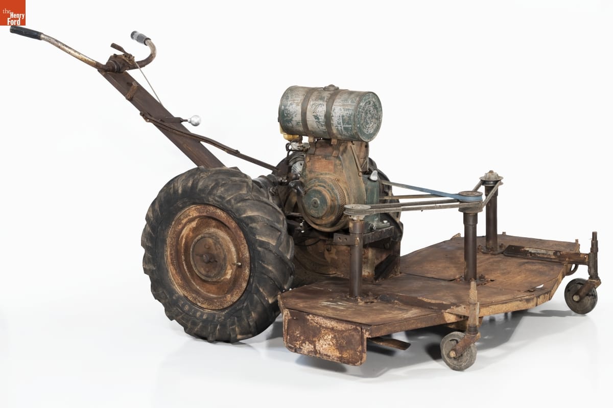Rough lawnmower with flat attachment and two small wheels in front; two large wheels behind; and crude handlebars
