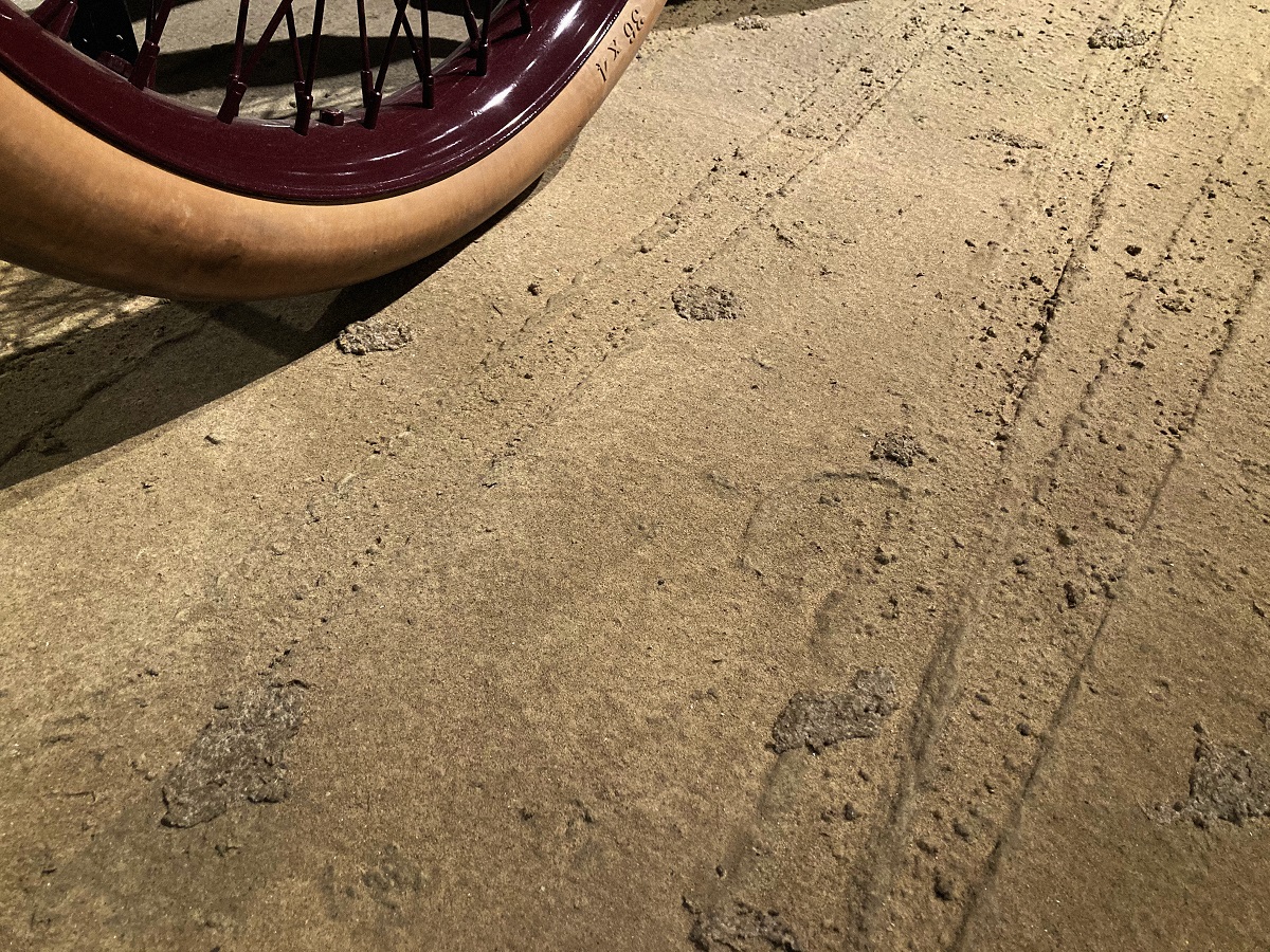 Dirt-looking surface with tire tracks and hoofprints built in; part of tire visible in corner of photo