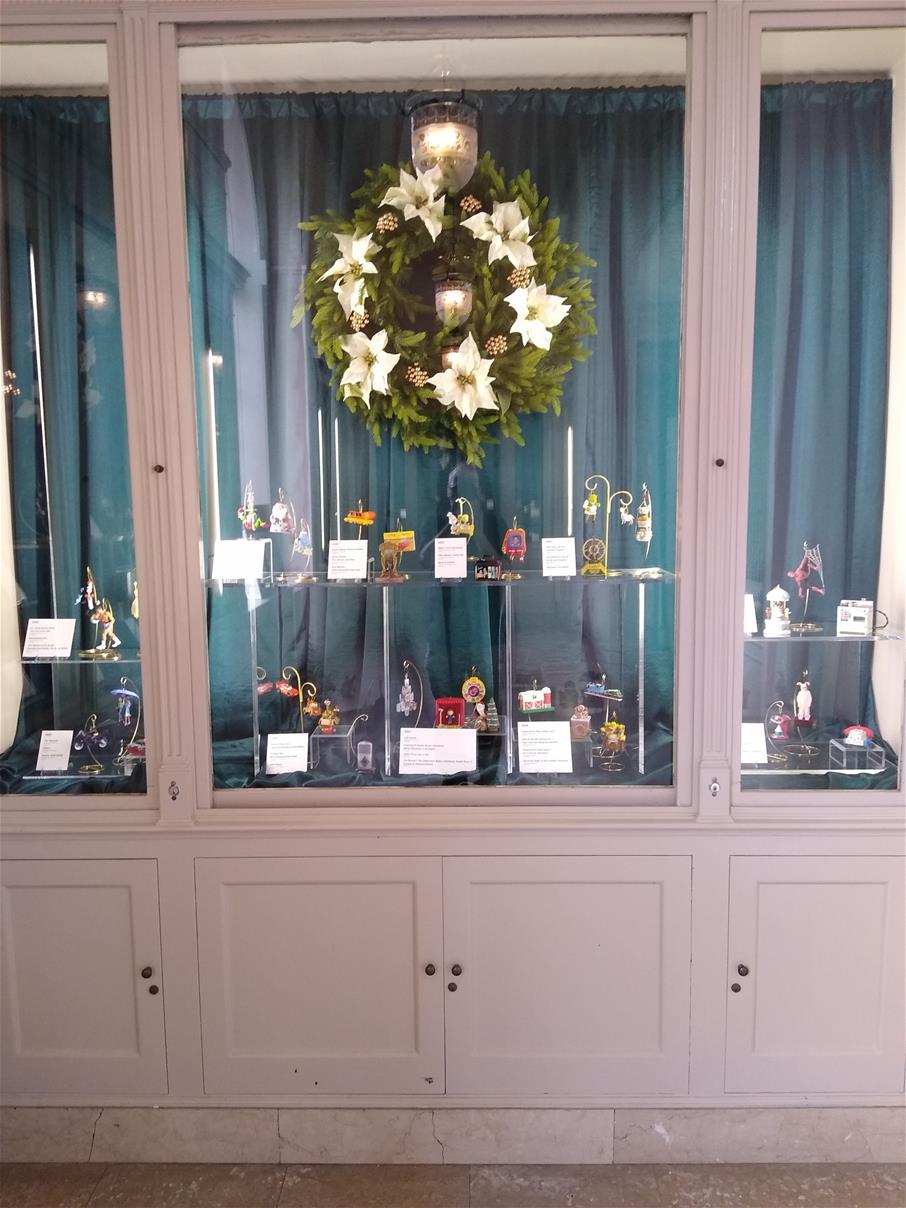 Though the Years with Hallmark: Holiday Ornaments exhibit in Henry Ford Museum of American Innovation Cabinets with blue curtains, with hanging Christmas wreath and ornaments on stands