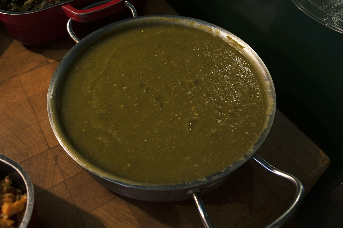Silver dish with handles, containing green sauce, sitting on butcher block
