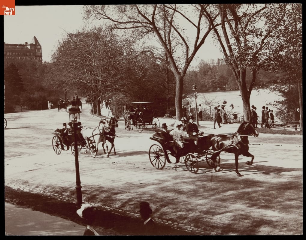 Horse-Drawn Vehicles on a Driveway, Central Park, New York City, circa 1900 Horses pull carriages along a road or drive, with pedestrians strolling underneath trees by a lake nearby