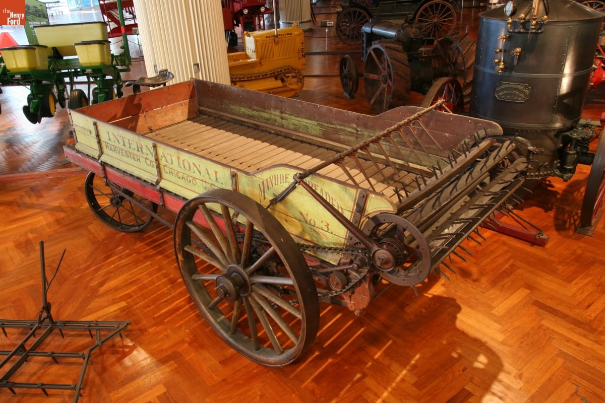 International Harvester Manure Spreader, circa 1905 Yellow wooden cart with text on the side with a large wooden beater at one end