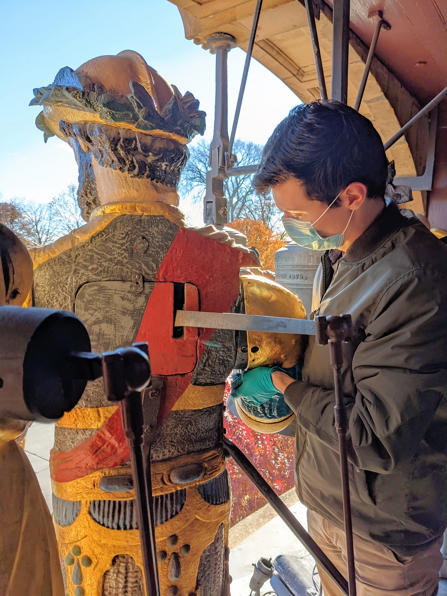 Person wearing mask holds a portion of a painted statue