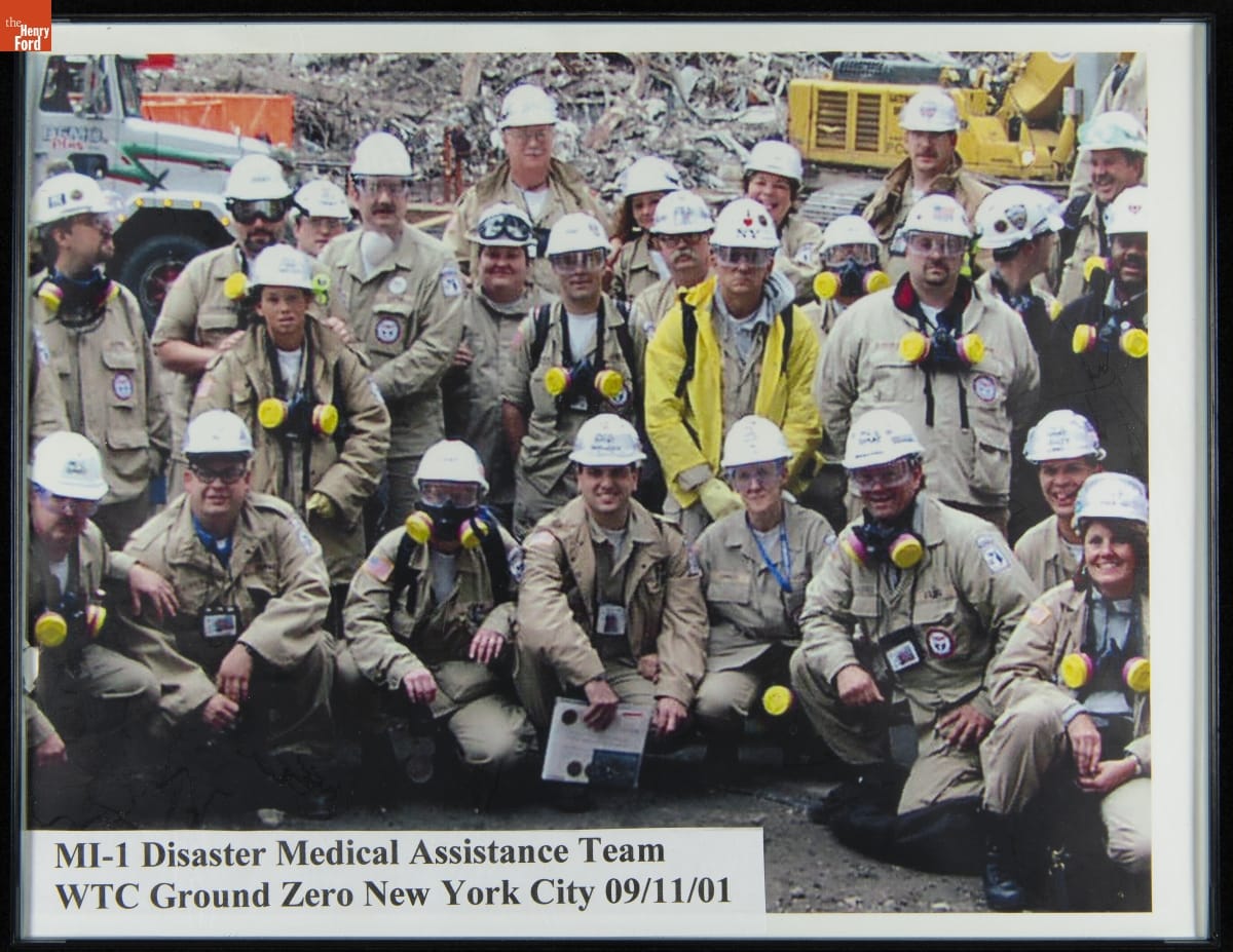 "MI-1 Disaster Medical Assistance Team, WTC Ground Zero New York City 09/11/01," 2001 Group of people, mostly in hard hats and khaki clothing, many with respirators, pose in front of a pile of rubble and construction equipment
