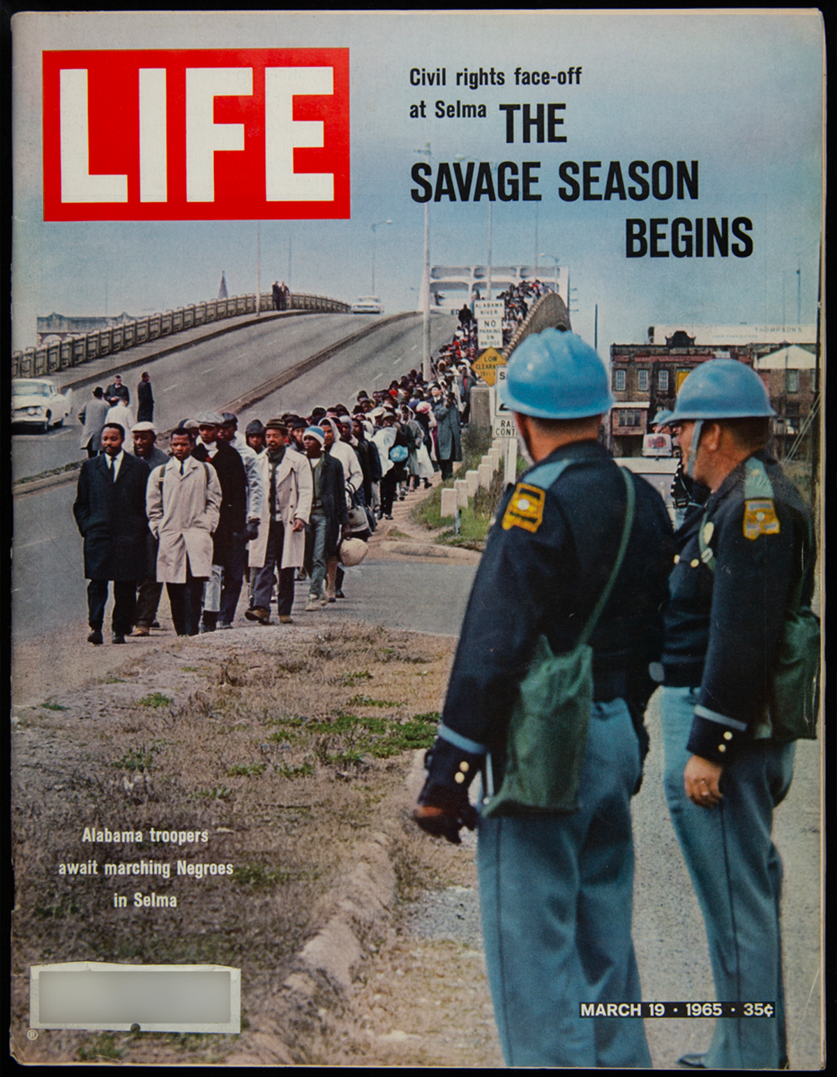 Cover of a magazine featuring Martin Luther King Jr. and fellow protesters walking along a highway with two police officers watching